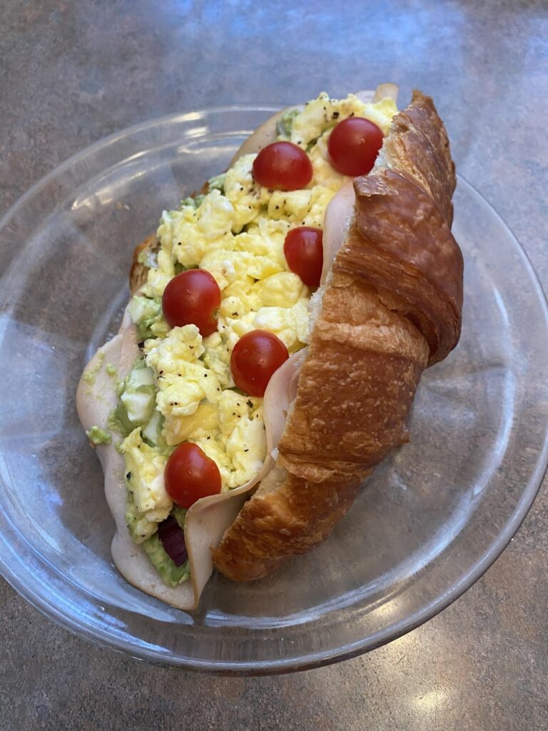 Avocado egg salad with Turkey and scrambled egg on top croissant breakfast sandwich