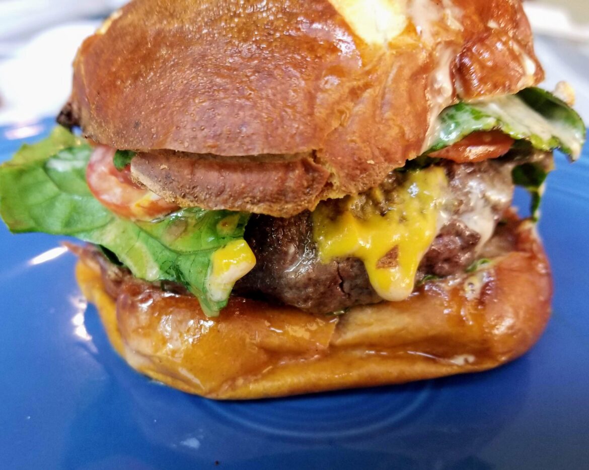 Burger with Cheddar, romaine lettuce, horseradish mustard and pickled Hungarian sweet peppers, on a pretzel bun