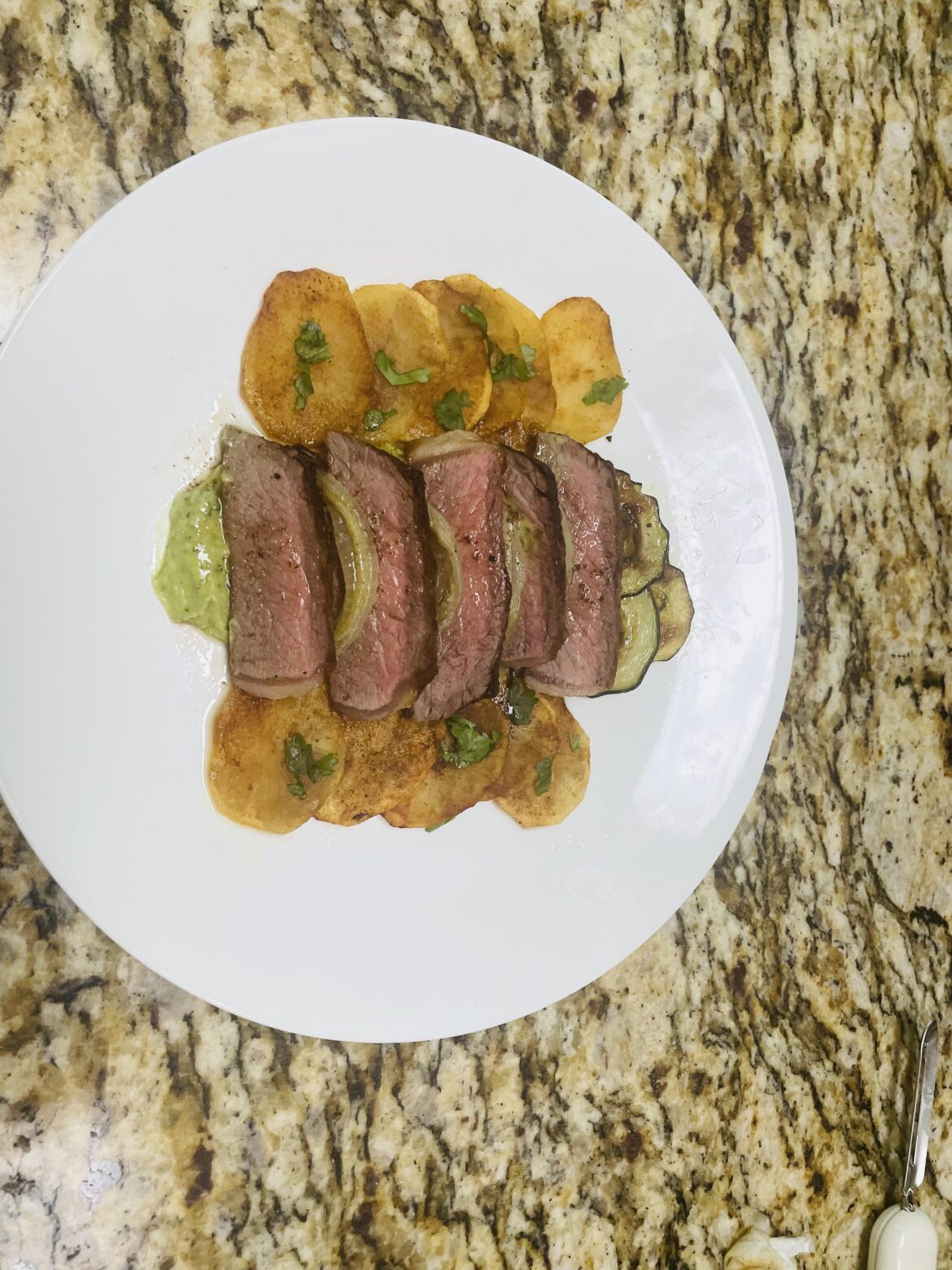 Steak with roasted potato, zucchini, and onion over an Advocado crema.