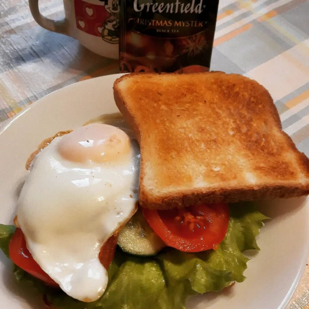 Toast with fried egg, cottage cheese, lettuce leaf and tomato and cucumber slices
