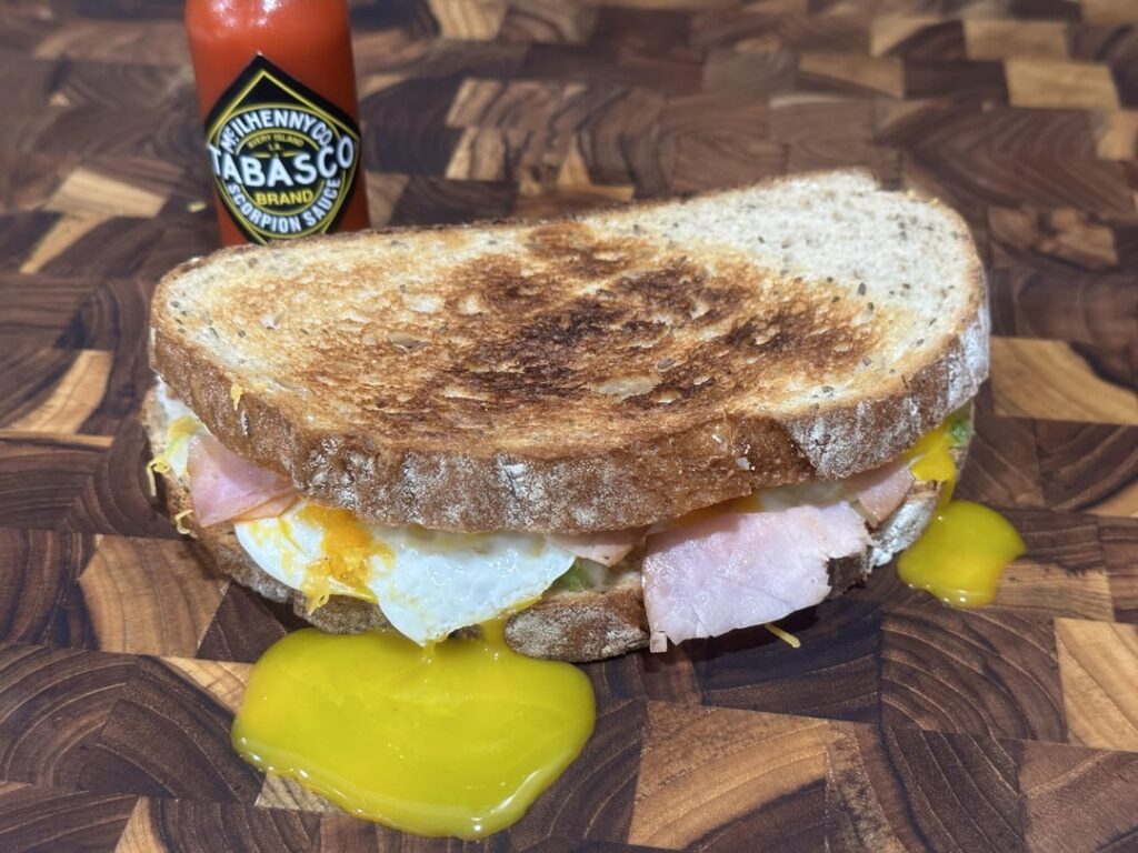 spicy egg sandwich: over easy eggs on rye toast, mayo, minced onion and jalapeño, fried ham, cheddar and hot sauce.