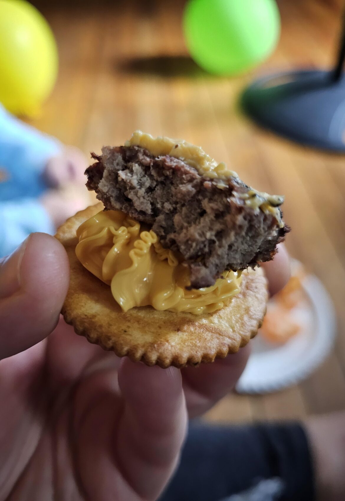 Veggie flavored Ritz cracker with squeeze cheese and a piece of cheeseburger on top