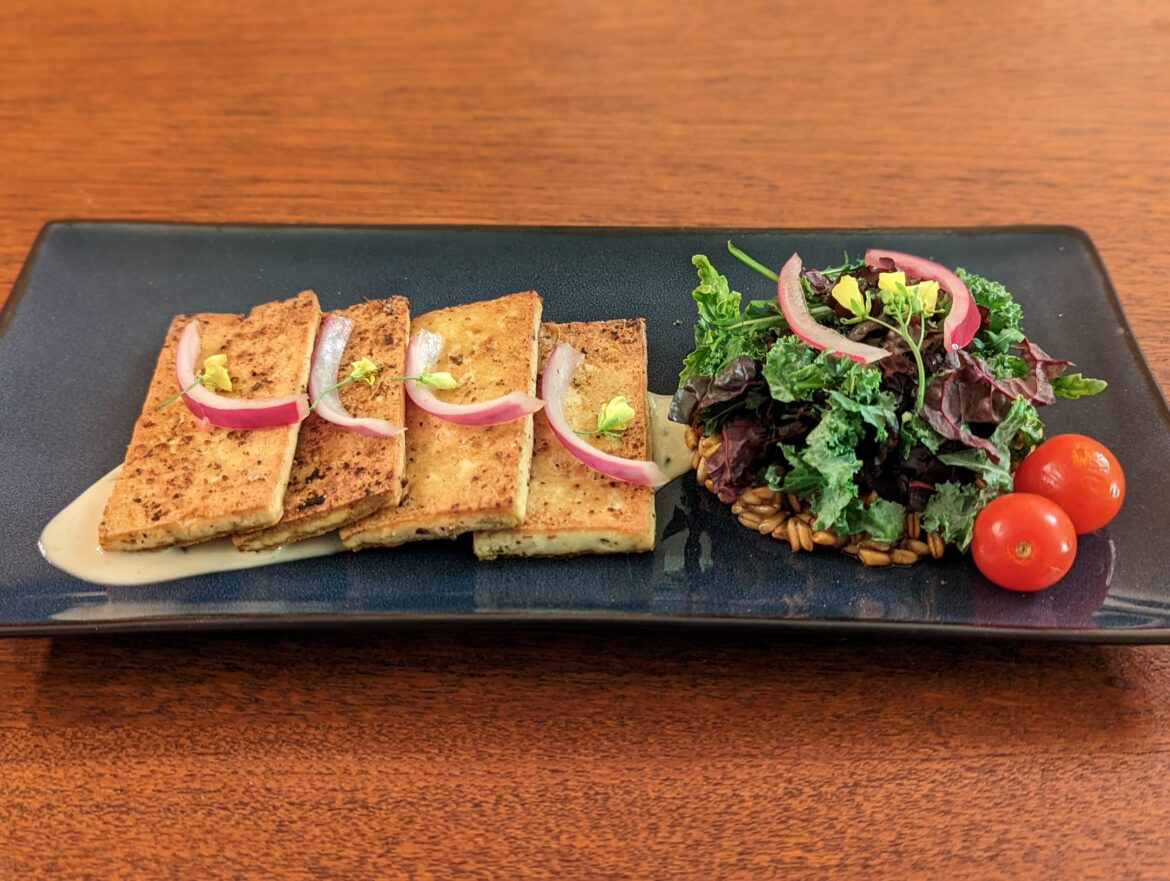 Mediterranean seared tofu with a farro and garden greens salad served on a lemon herb tahini dressing