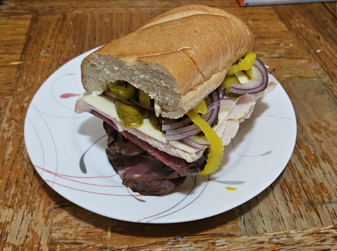 Roast beef, turkey, pepper jack, pickles, red onion, banana peppers, mayo and dijon mustard on a loaf of French bread.