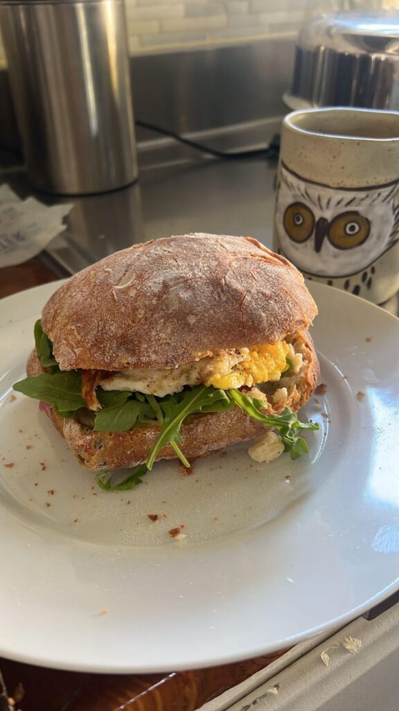 Fried egg cooked with sartori montamore cheese, evoo, garlic powder, salt, paprika, green chile flakes, pepper, and butter on an olive roll, with pickled onions, arugula, butter, and sartori montamore