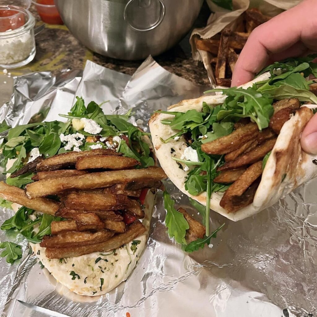 garlic naan wrap with Hellman mayo, sriracha, cucumber, dill, roasted red pepper, Greek feta, fries, arugula, and an avocado dip made with carrots, habanero, raw garlic, raw red onions, flavortown cherry tomatoes, sautéed red onions and garlic with passion fruit chili pepper salt, and pepper