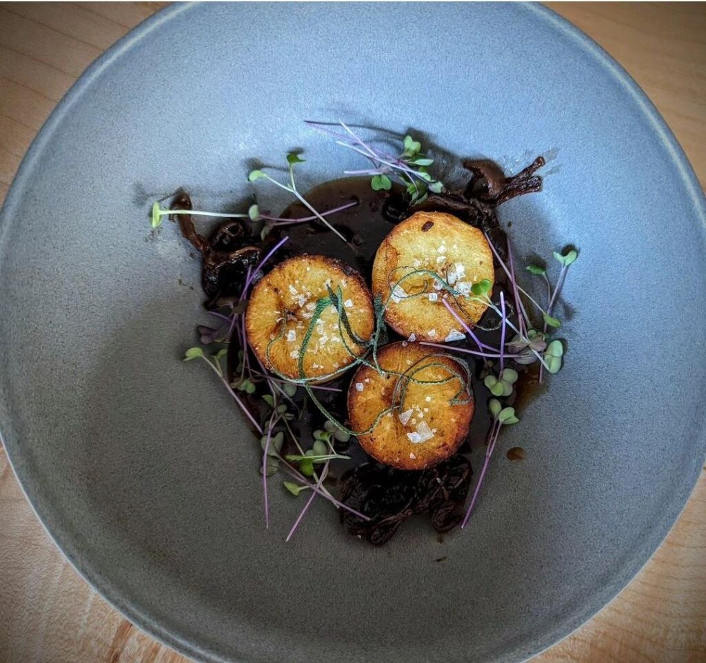 Fondant potatoes with vegan demi, rye whisky caramelized onions, sage, and radish micros