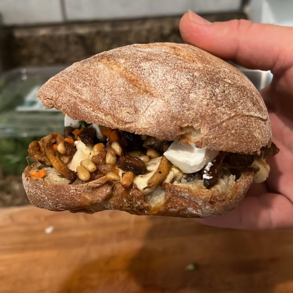 Shiitakes sandwich on an olive roll with garlic hummus, schug, toasted pine nuts, barrel aged Greek feta, and diced cucumber and carrot