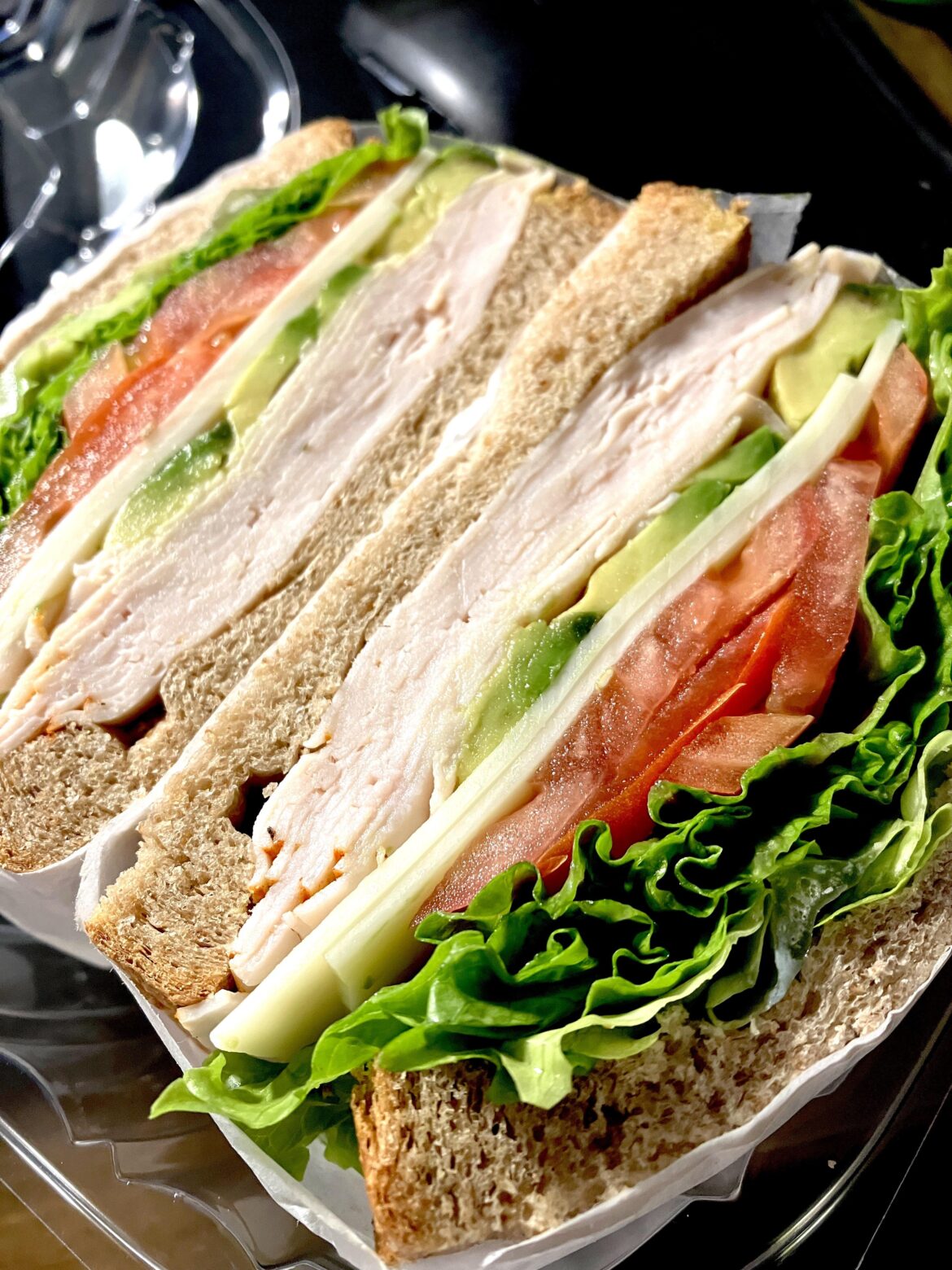 Turkey sandwich with tomato, lettuce, avocado, and Swiss cheese on whole wheat.