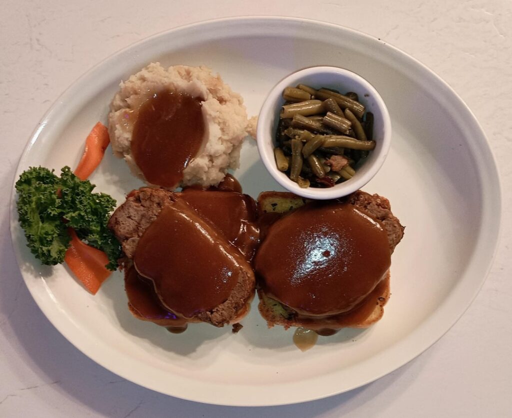 ' Dinner #1' Open faced Meatloaf Sandwich on Garlic Toast with Brown Gravy. Side of Mashed Potatoes and Gravy, Dinner Veggies (Green Beans, Onions and Bacon)
