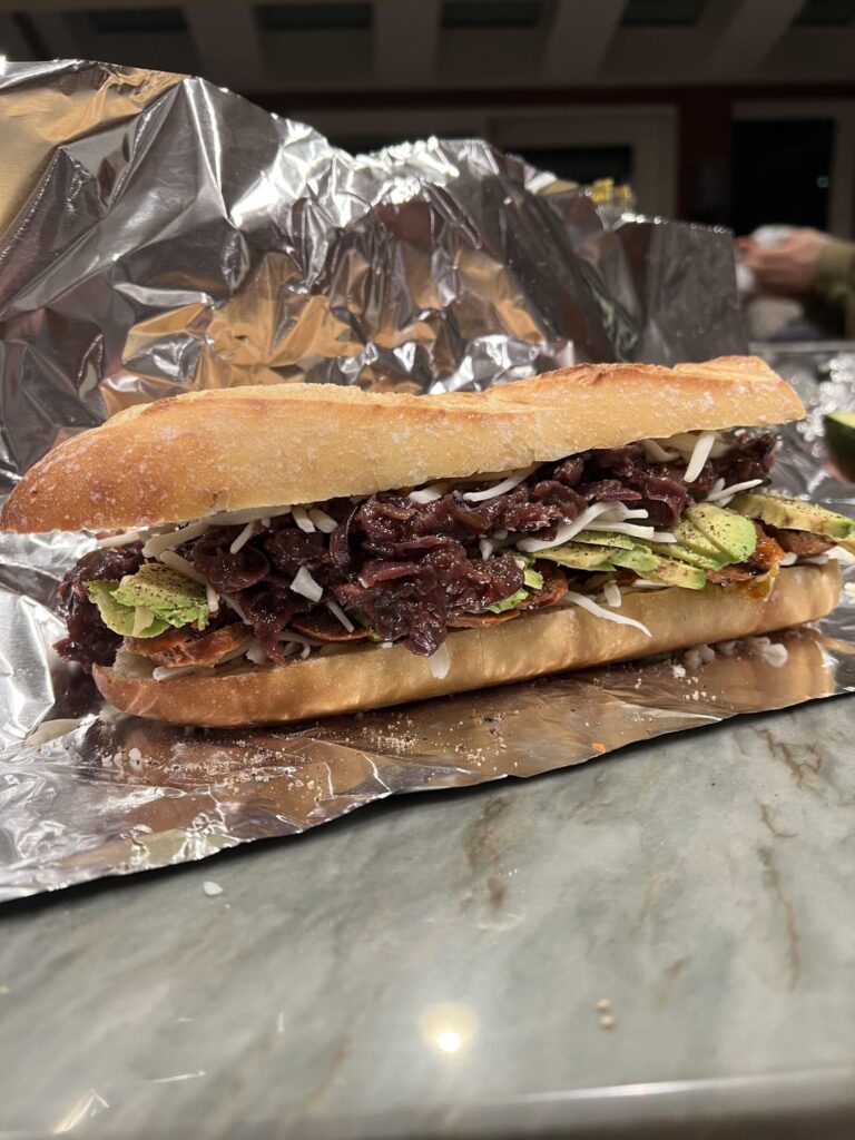 Italian sausage sandwich with goat cheese, sambal oelek, balsamic vinegar, Hot giardineira, dressed avocado, braised cabbage and mushrooms