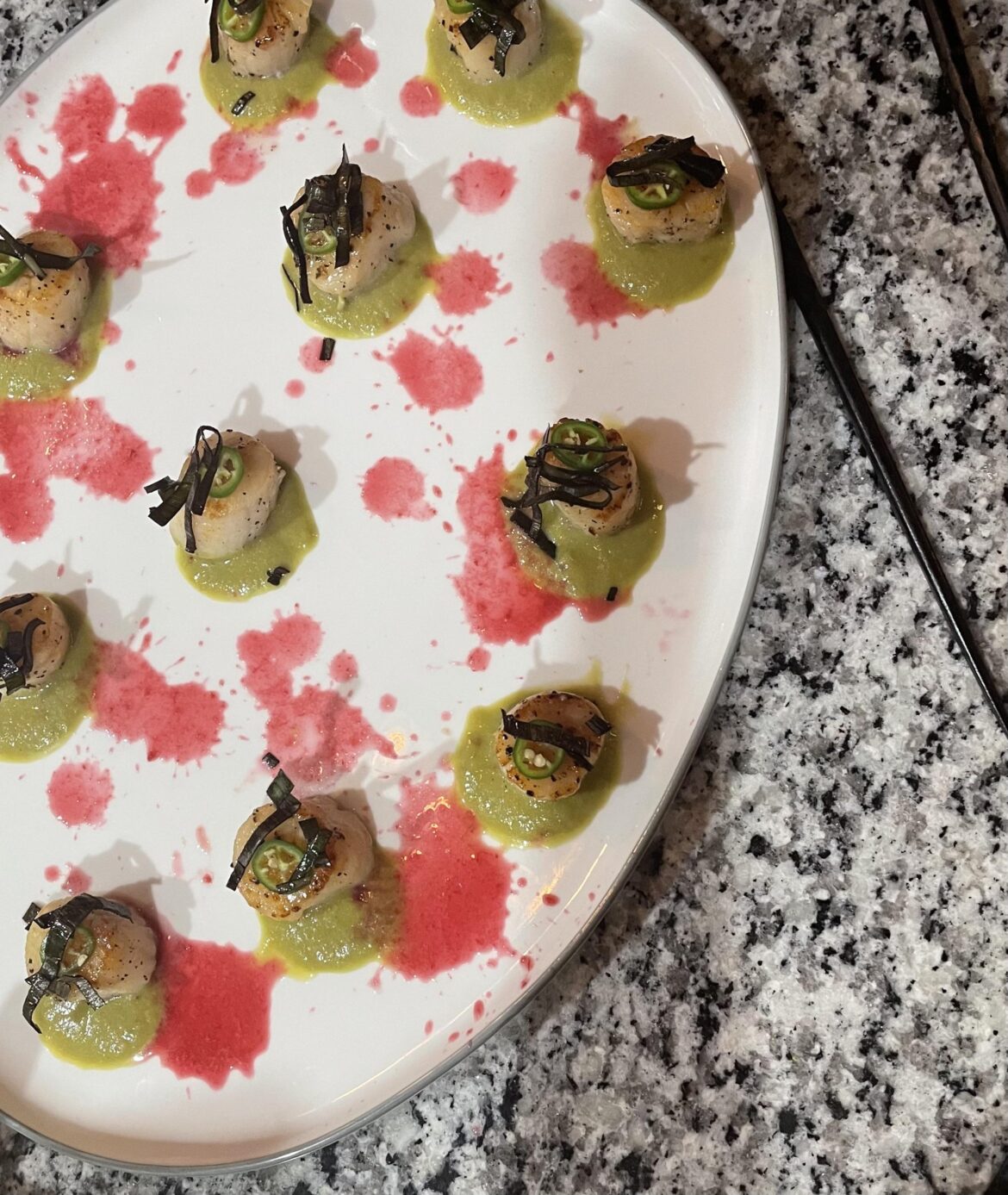 Seared scallops over leek and starfruit purée and pomegranate juice, topped with Serrano and flash fried leeks