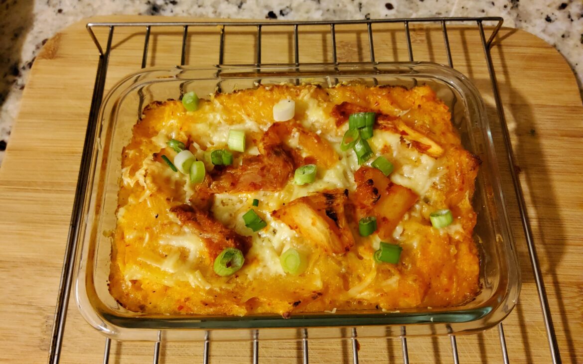 A single serving of baked mashed potatoes with kimchi and grated cheddar cheese.