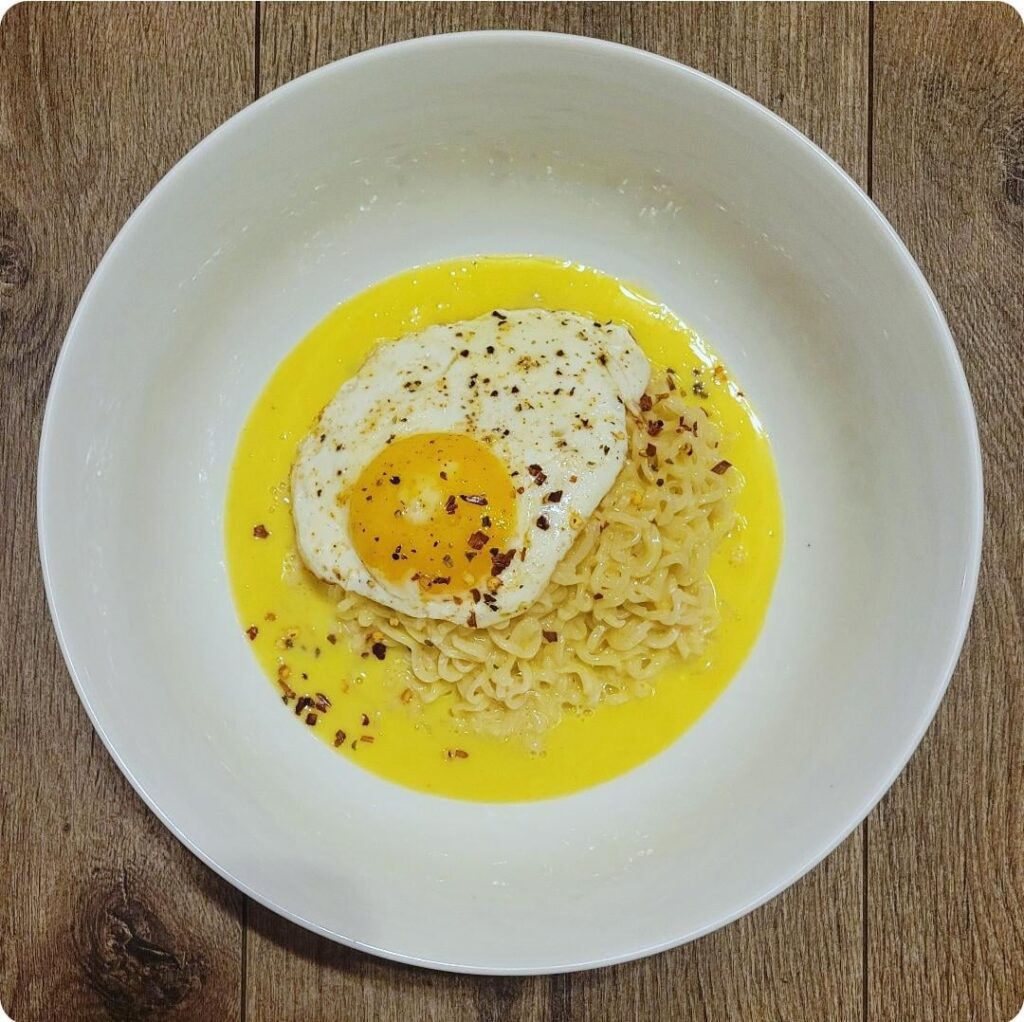 Instant chicken ramen in cream sauce, topped with sunny-side-up egg and chili flakes.