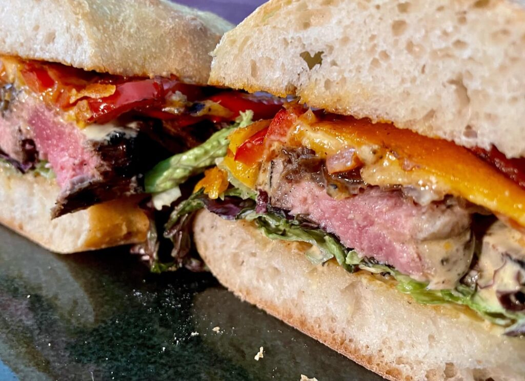 Steak sandwich with melted cheese on bell peppers, caramelized onion chutney and mustard mayo