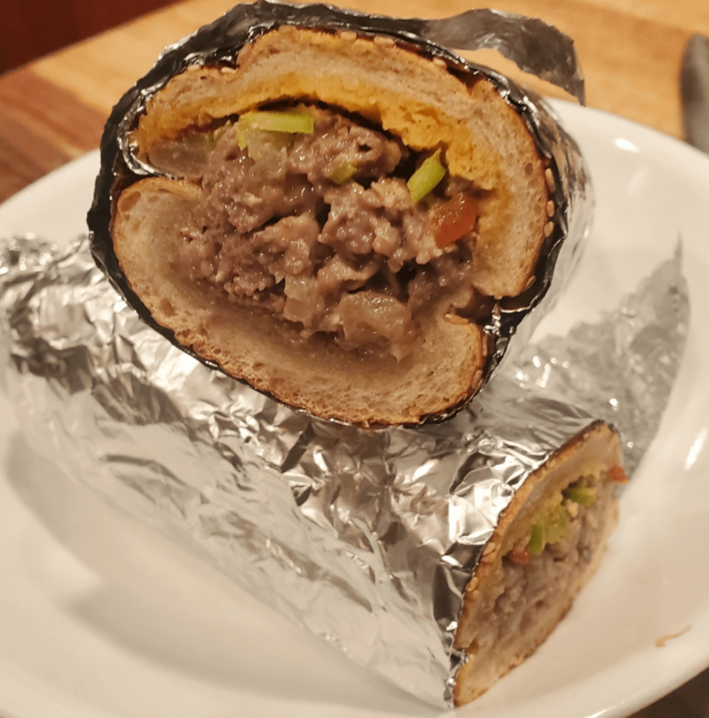 Philly Steak: Shaved Ribeye, American & Sharp Provolone, Caramelized Onion, Cherry Pepper, Calabrian Chili Oil, Seeded Semolina