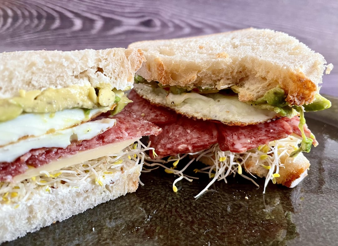Breakfast sandwich with fried eggs, salami, gouda cheese, alfalfa