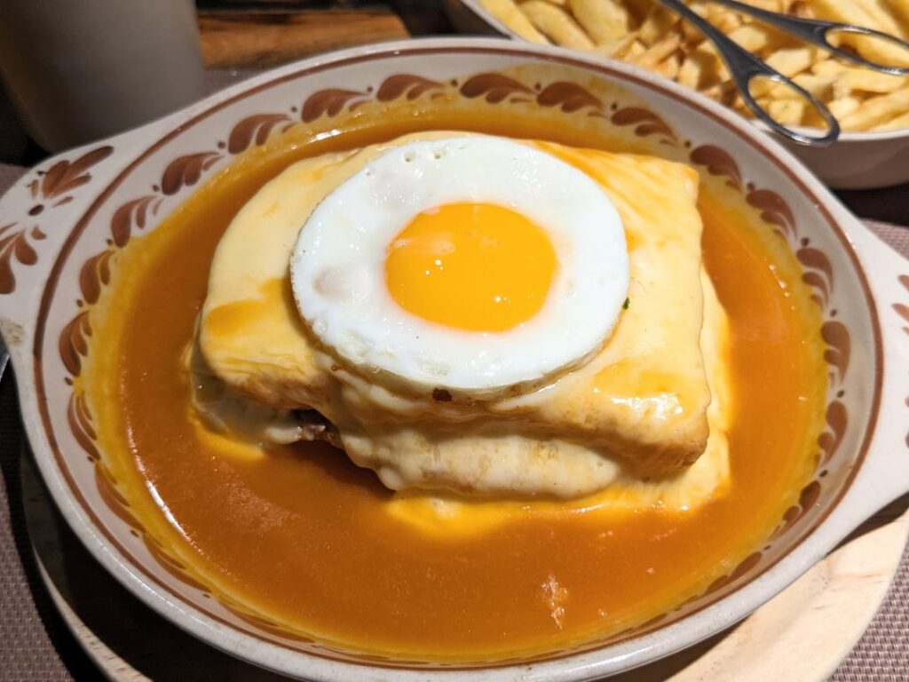 The Francesinha - white bread, fresh sausage , ham , cold cuts and beef steak , covered with melted cheese . It is garnished with a tomato , beer and piri-piri sauce. From Brasão in Porto, Portugal.