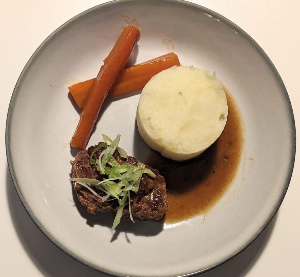 Porter-braised pork cheeks and reduction, braised carrots, garlic mashed potatoes, spring onions