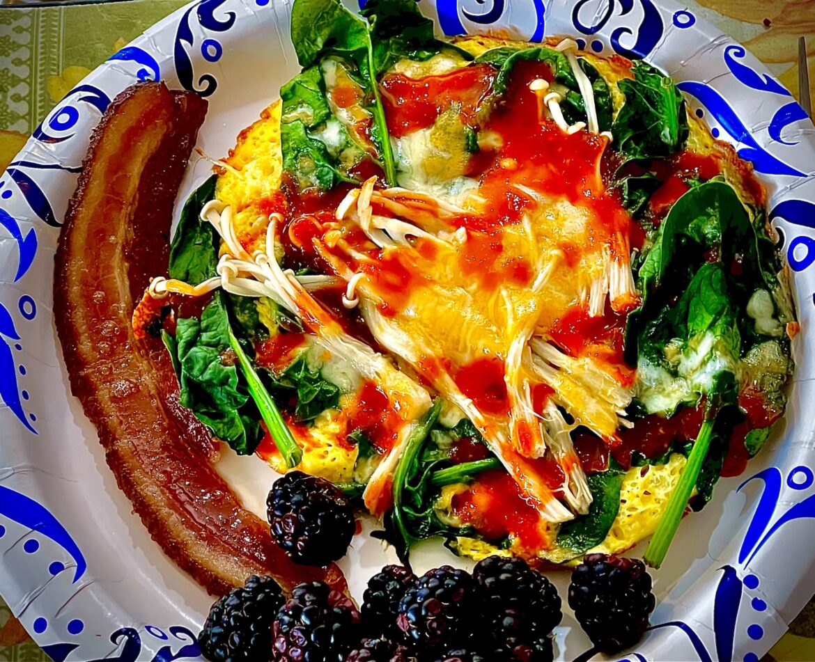 A delicious breakfast Farm fresh eggs with spinach, enoki mushrooms, homemade bacon, Colby Jack cheese, a splash of homemade chili sauce, and a hand full of blackberries