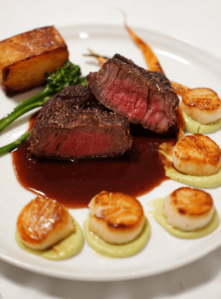 Filet mignon with a red wine reduction sauce, seared scallops over avocado puree, roasted broccolini and carrots and potato pave