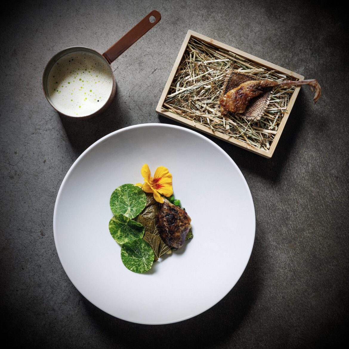 Grilled leg (including the foot and the claws) served on a piece of hemp cloth, on a bed of dried crop residues, inside a bamboo box from IKEA