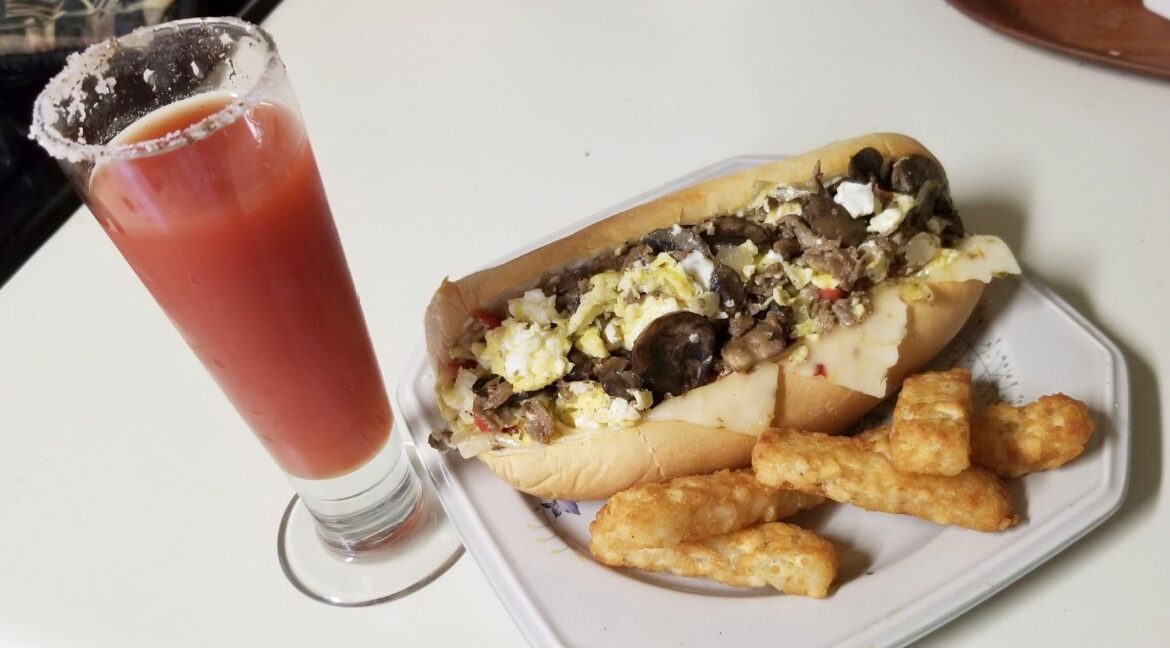 A Breakfast Cheesesteak. Shaved sirloin, mushroom, red bell, onion, egg, and ghost pepper cheese on a toasted Martin's potato hoagie roll. With Hash brown sticks and a bloody Cesar for dipping and sipping.