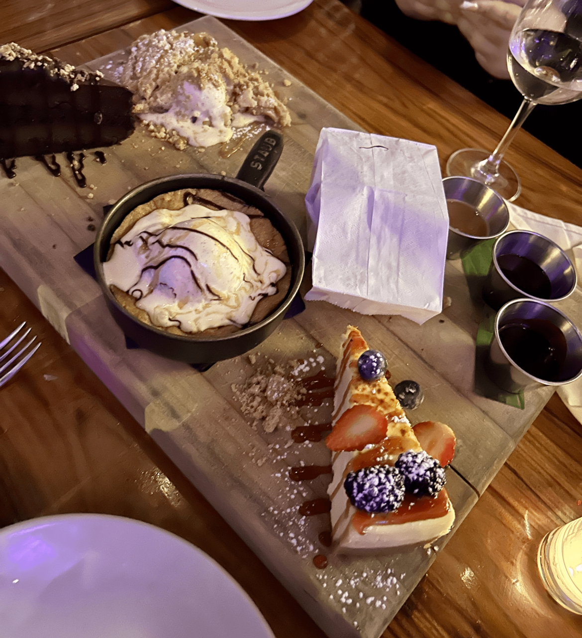 Melting ice cream and other desserts on a singular cutting board for the whole table to use but donuts are in a bag