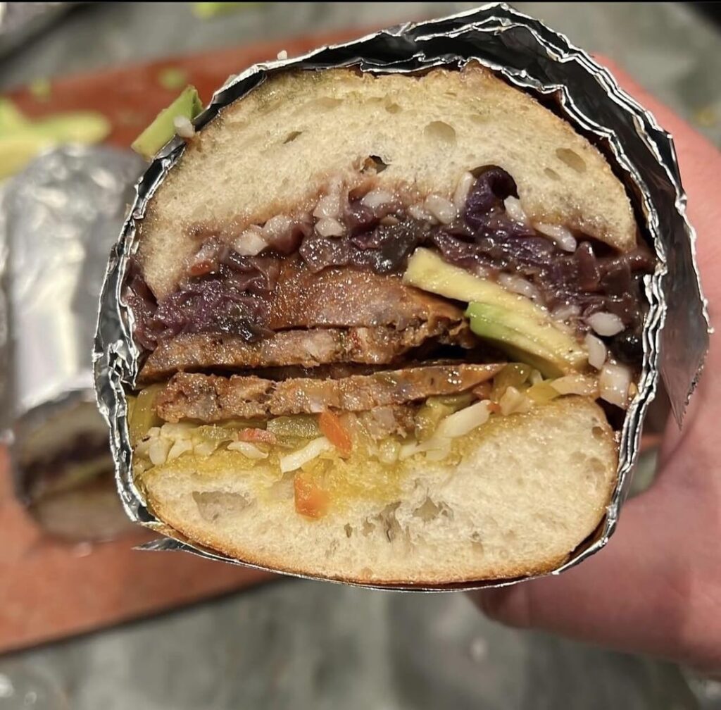 Italian sausage sandwich with goat cheese, sambal oelek, balsamic vinegar, Hot giardineira, dressed avocado, and red cabbage red onion cremini mushrooms and Granny Smith apple slaw
