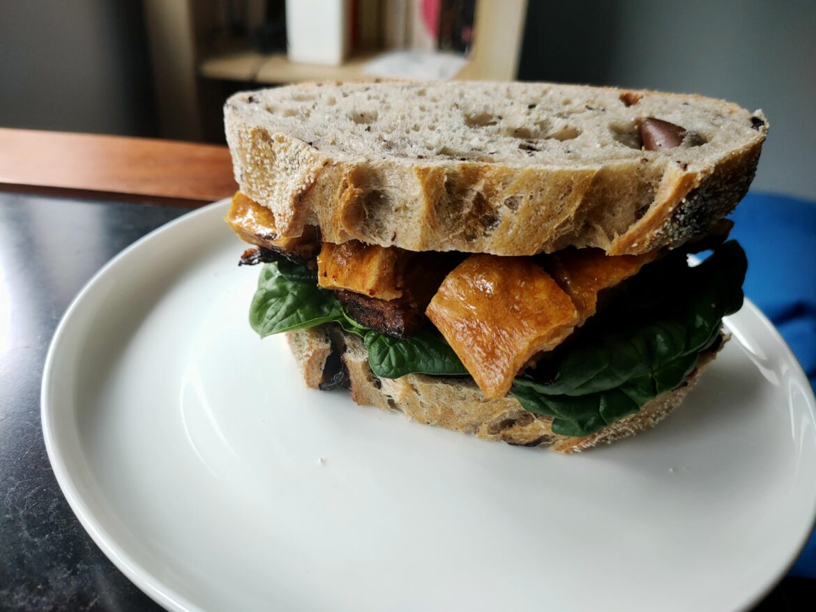 Crispy coffee rubbed pork belly with baby spinach and sriracha on Kalamata olive sourdough