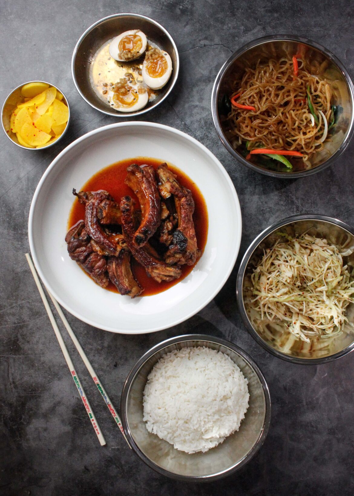 Kimchi braised pork ribs with banchan (sweet-pickled daikon, jjapchae, soy marinated eggs, spicy cabbage and rice)