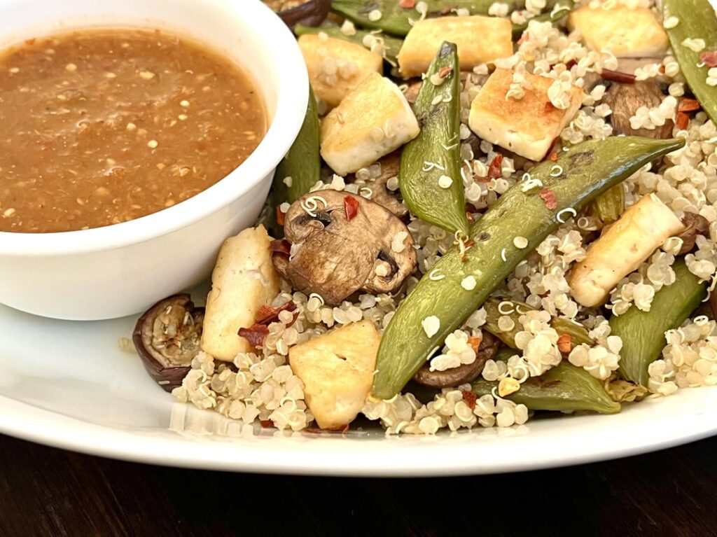 Quinoa stir fry with pan-roasted tofu, mushrooms and sugar snap peas. Served with tomato hempseed sauce.