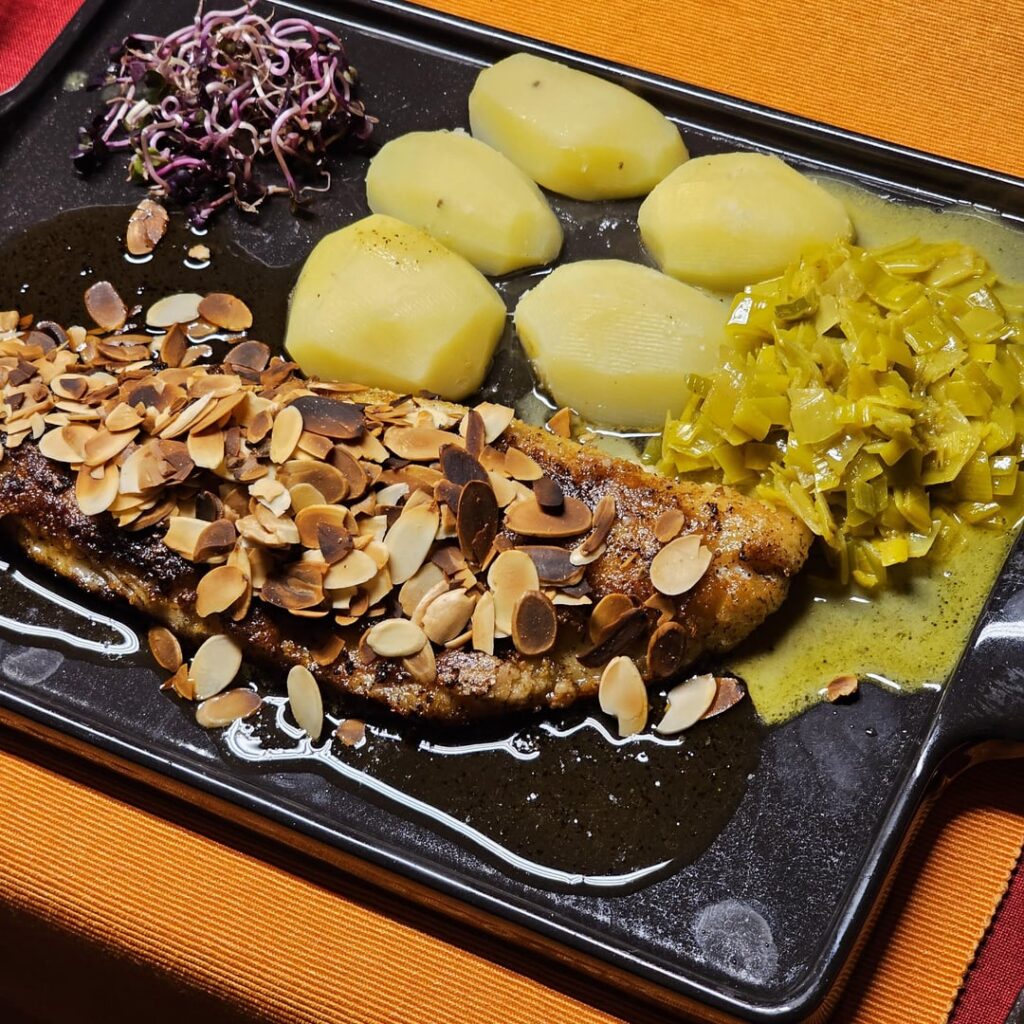 Fried fillet of pike-perch with roasted almonds in a lemon-butter sauce, with leek in a curry-white wine sauce, boiled potatoes and red radish sprouts