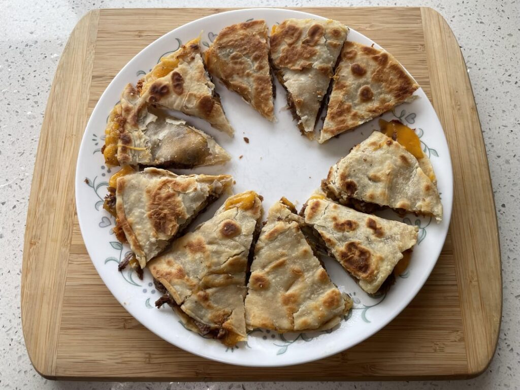 [Homemade] A gourmet quesadilla featuring house-made flour tortillas, slow-cooked shredded pot roast, seasoned black beans, and a melty blend of pepper jack and sharp cheddar cheese, all finished with a crisp, buttery crust. And a side of my homemade Guacamole Salsa