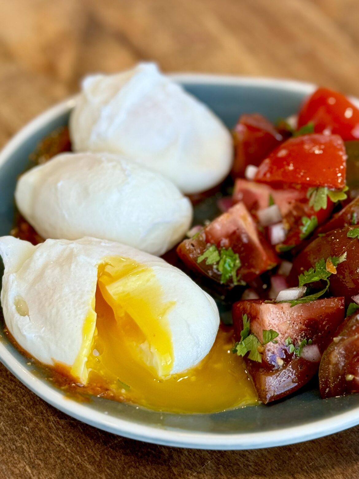 Poached eggs over harissa-mustard hot sauce alongside tomatoes tossed in red onion and cilantro