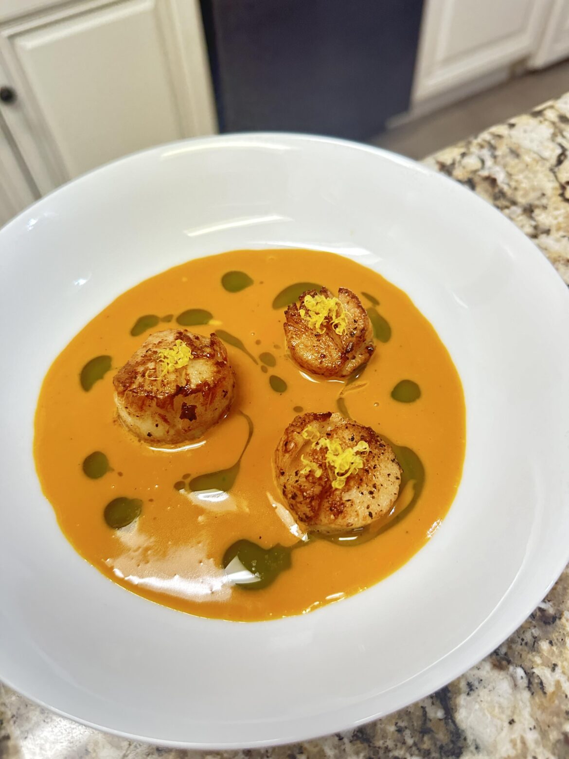 seared scallops with a carrot beurre blanc and parsley oil garnished with lemon zest