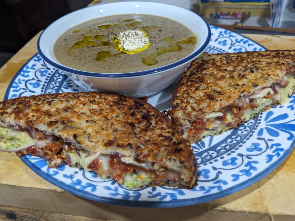 Sundried tomato, red onion, avocado and tripple cream brie toasted sandwich on soy and linseed bread served with a six kinds of mushroom soup garnished with finishing olive oil, sour cream and cracked black pepper.