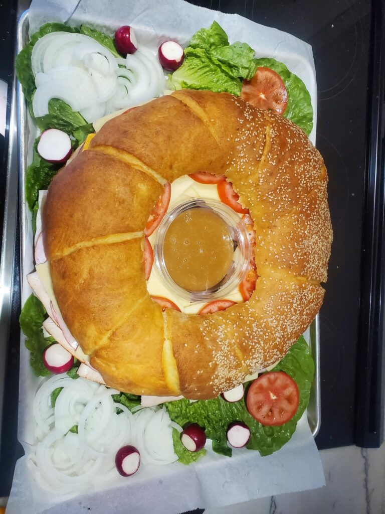 New member of the family. 8lbs, 14". Homemade round bread half sesame seed. Turkey, ham, cheddar, Swiss, lettuce, tomato. Spicy honey mustard in the middle.