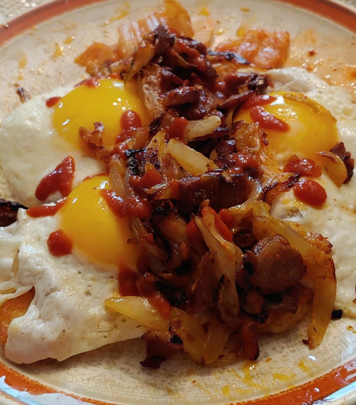 Sliced leftover Viet pork chop, onions, kimchi over three sunny eggs. Crispy potato rounds underneath