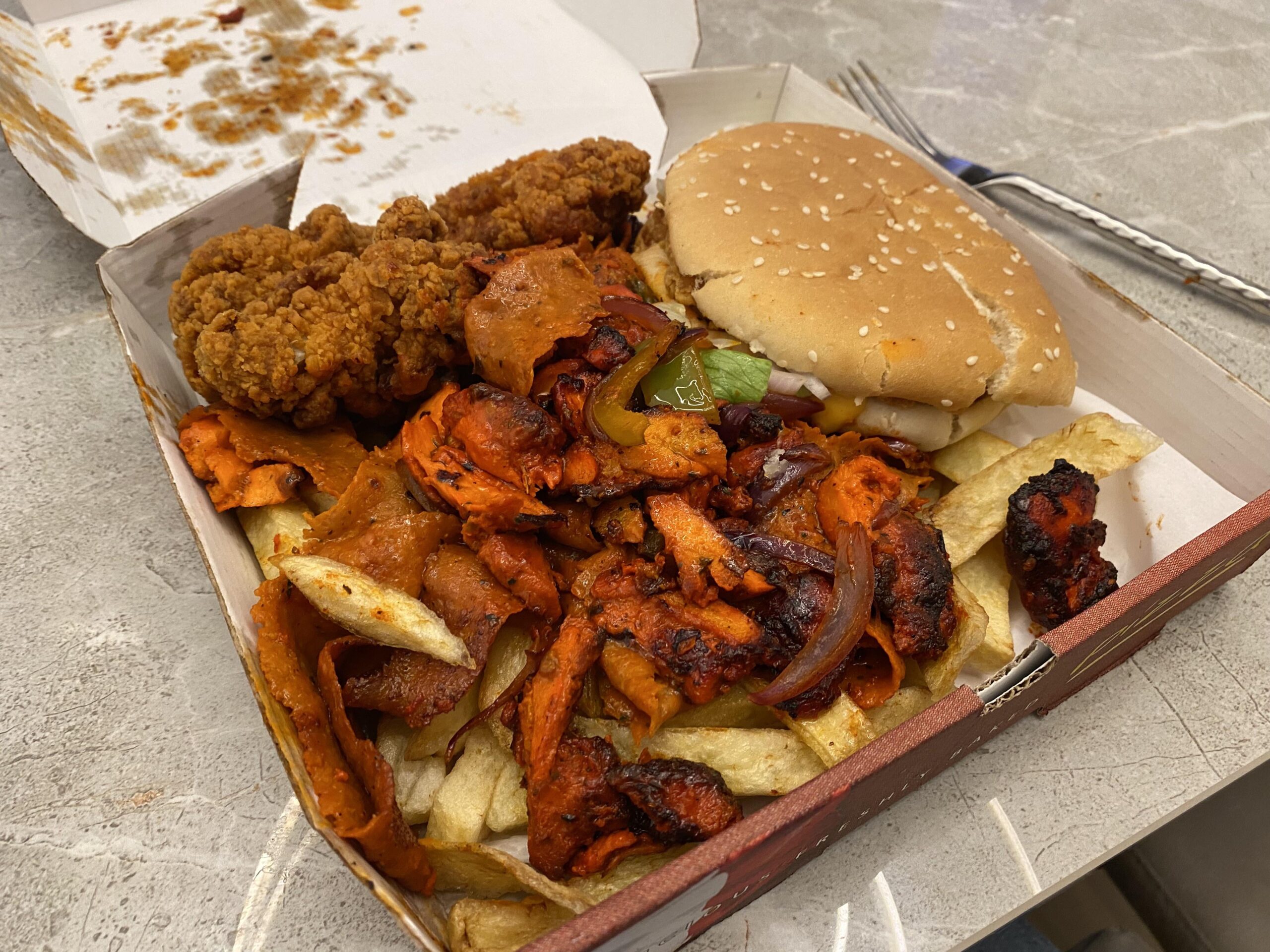 A tasty platter of chicken burger, spicy chicken wings, and spicey donner meat mixed with chips