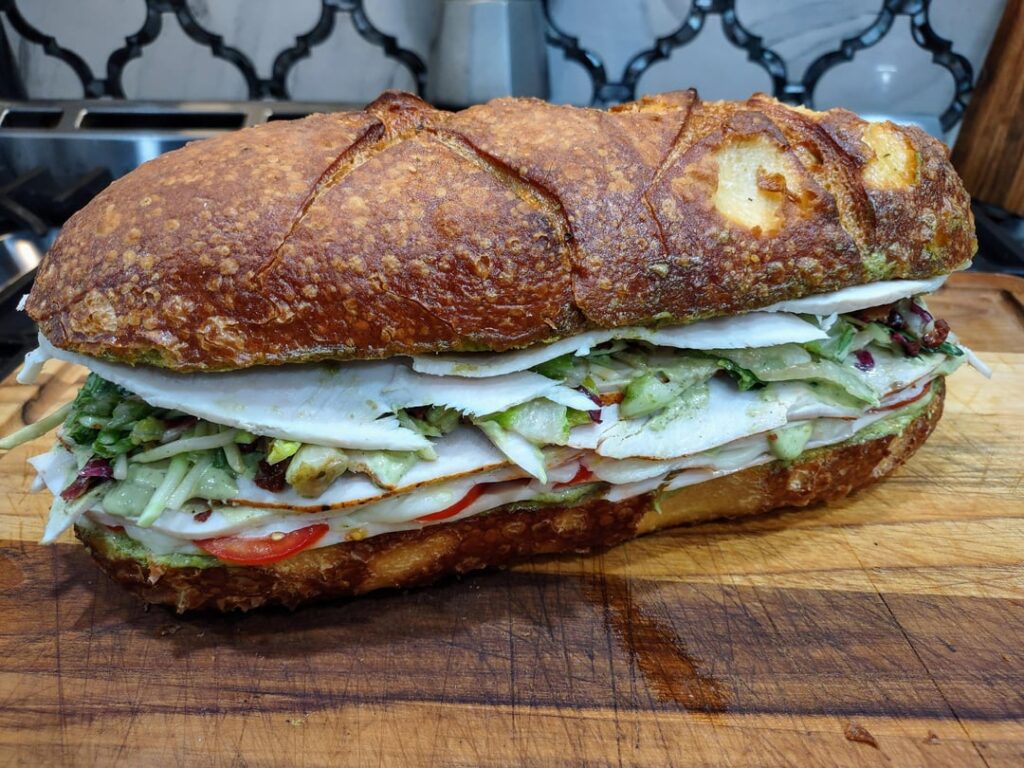 Homemade Deli Sandwich - Roasted Turkey, White Cheddar, Tomato, Shredded Lettuce and Red Cabbage Slaw, and Spicy Avocado Mayo on French Bread.