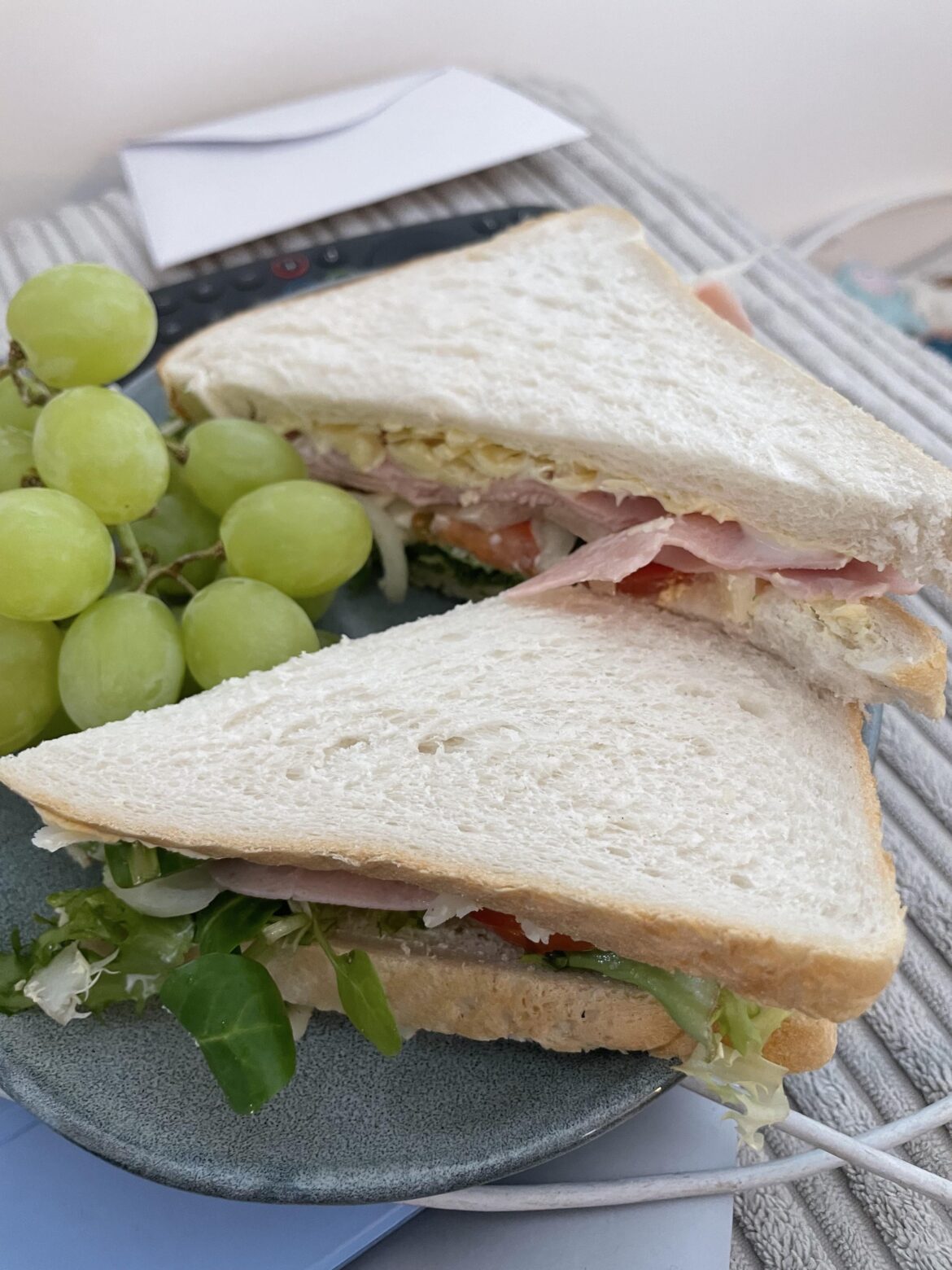 A simple ham and cheese salad sandwich with a side of grapes.