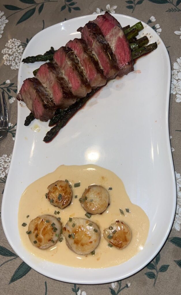 New York strip on a bed of pan seared asparagus and scallops in a white wine buerre blanc