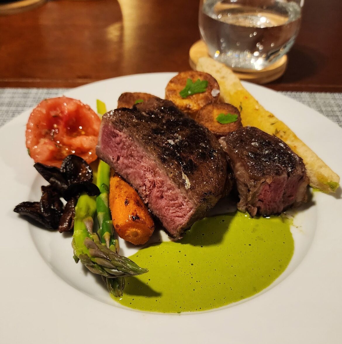 Grilled rib eye, chimichurri sauce, fondant potatoes, roasted tomato, asparagus, sauteed mushrooms and carrot.
