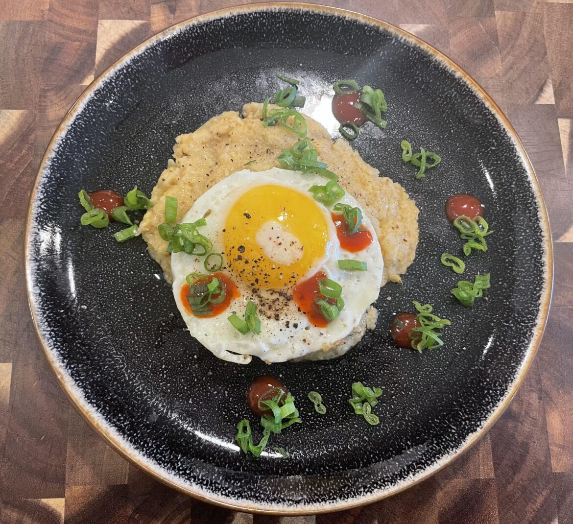Creamy polenta with a sunny side up egg, garnished with scallions and sriracha