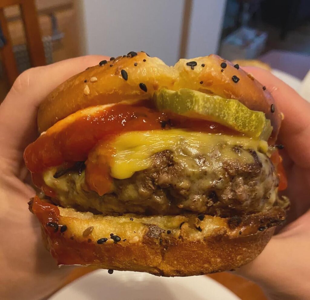 American cheese burger with spicy pickles on a toasted everything bagel brioche bun