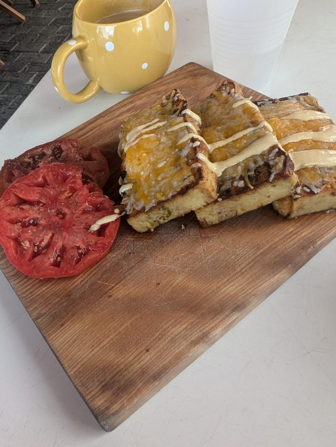 Bacon bread pudding and fresh tomato on a dingy used wood cutting board.