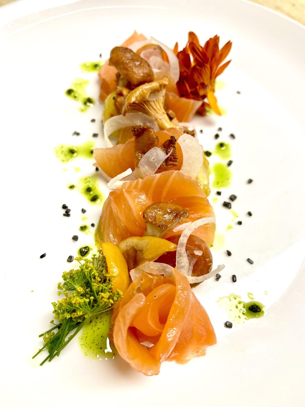 Fennel cured Royal Tide salmon. Confit grape tomatoes, Chanterelle mushrooms, shaved fennel, lava sea salt and herb oil.