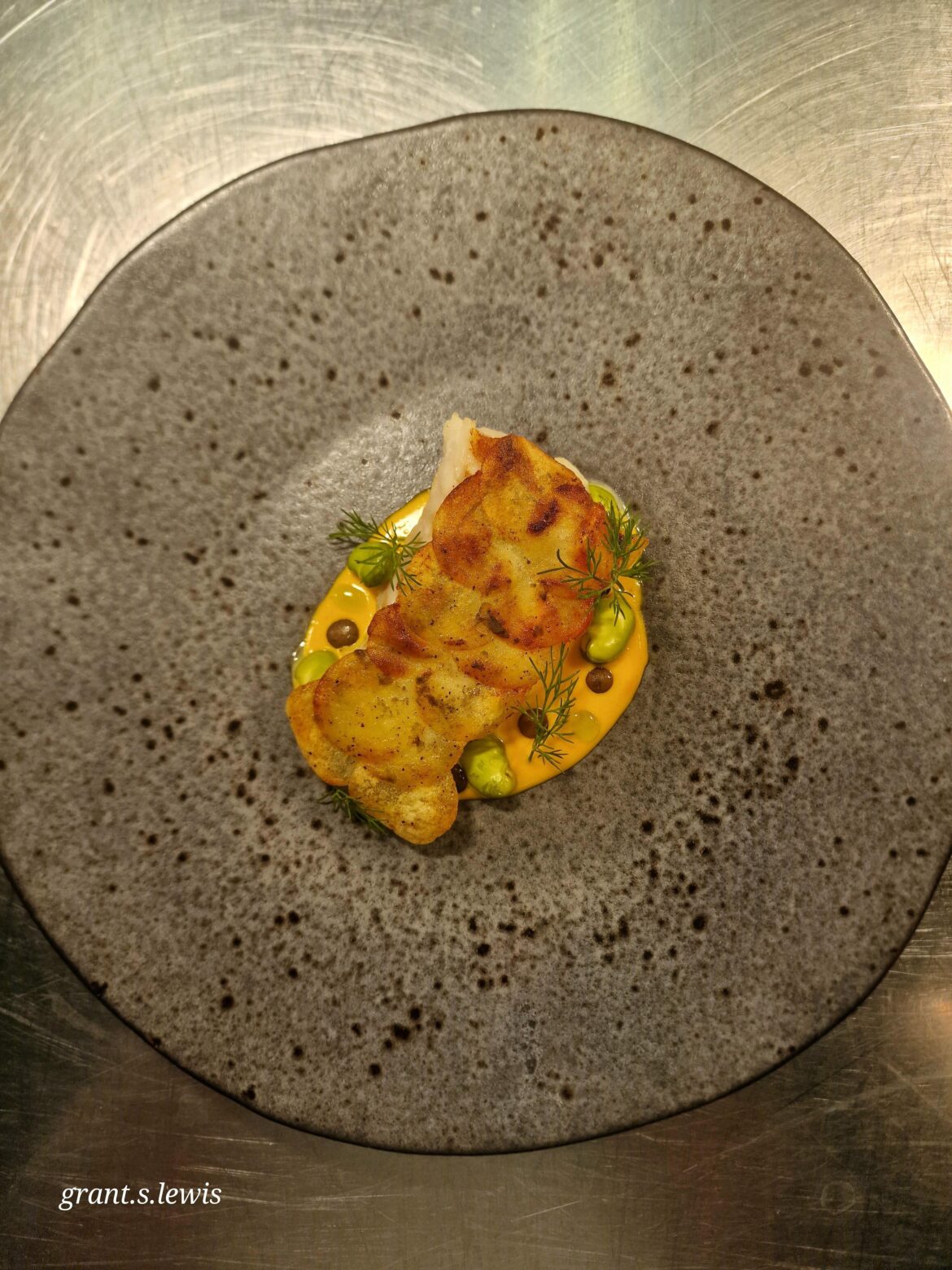 Hand seared cod with potato fish scales and saffron sauce with broad beans.