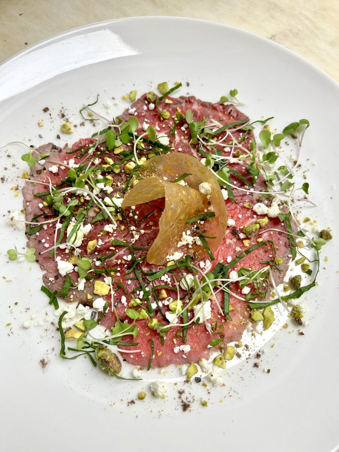 Beef carpaccio. Crumbed goat cheese, pistachio powder, kale, lava salt and orange tuile.